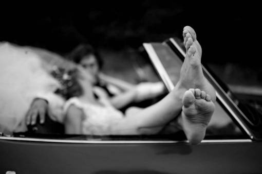 kiss legs barefoot married bride woman groom convertible outdoors — black and white photo